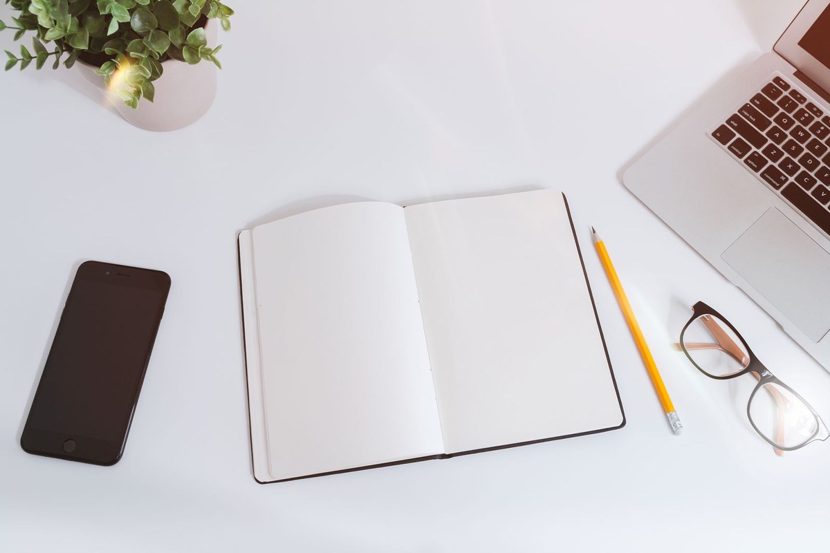 Bright, tidy desk with an open notebook, laptop, and smartphone.